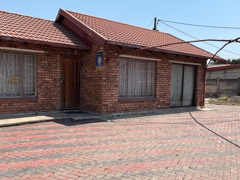 Front view of a single-story face brick house featuring a tiled roof, paved driveway, and security bars on windows.