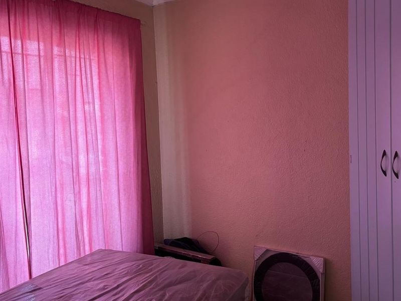 A bedroom featuring a built-in wardrobe and a large window with pink curtains, requiring cosmetic updates to the wall finishes.