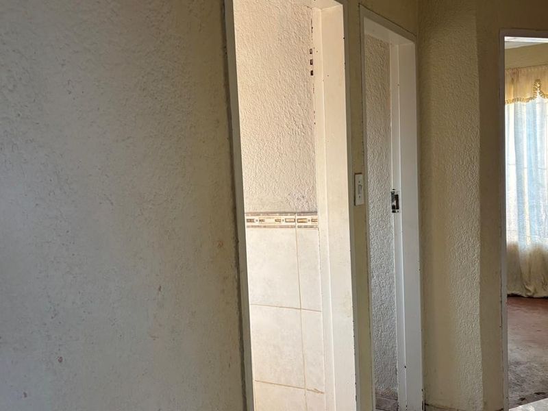 A view of a residential hallway showing multiple doorways and dated wall finishes, leading into adjacent rooms.