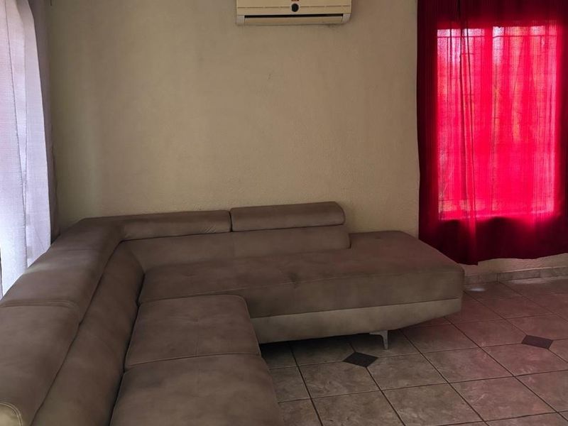 A living room area featuring tiled flooring, an installed air conditioning unit, and window security bars.