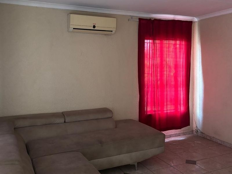 A living room featuring tiled flooring and a wall-mounted split-system air conditioner, requiring cosmetic updates to the wall finishes.