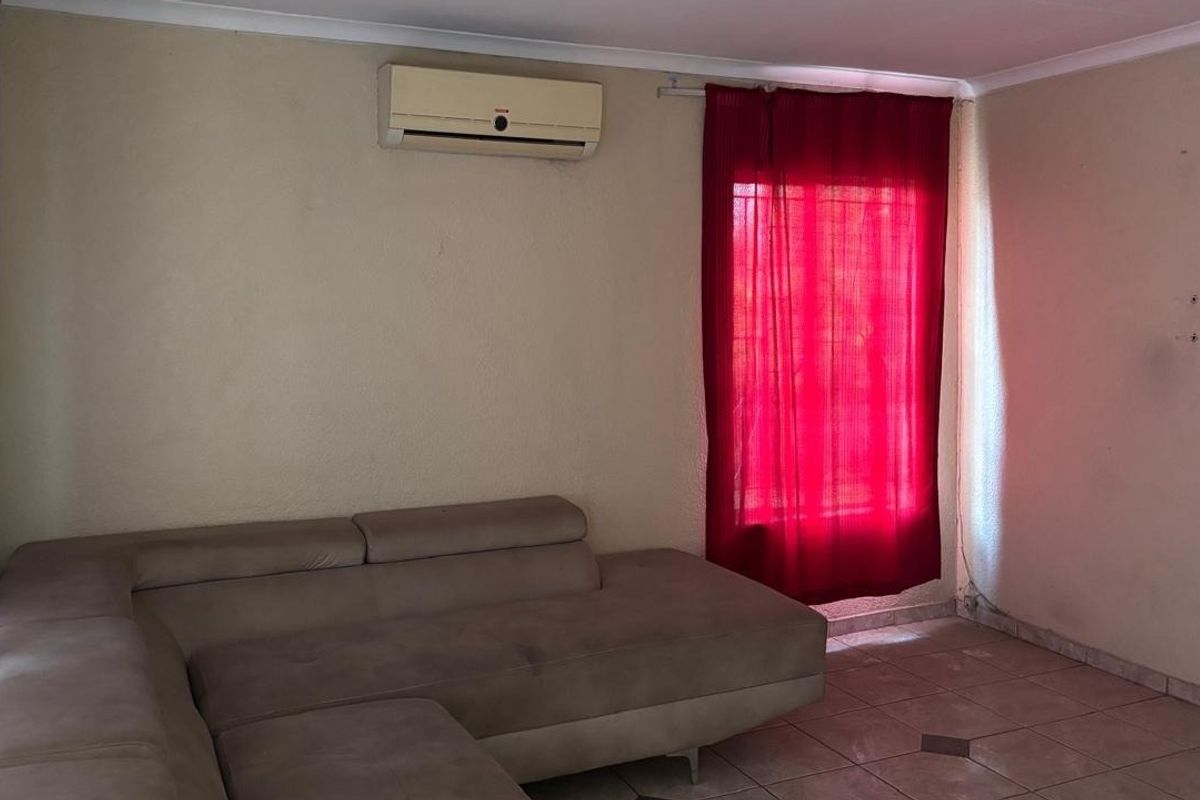 A living room featuring tiled flooring and a wall-mounted split-system air conditioner, requiring cosmetic updates to the wall finishes.