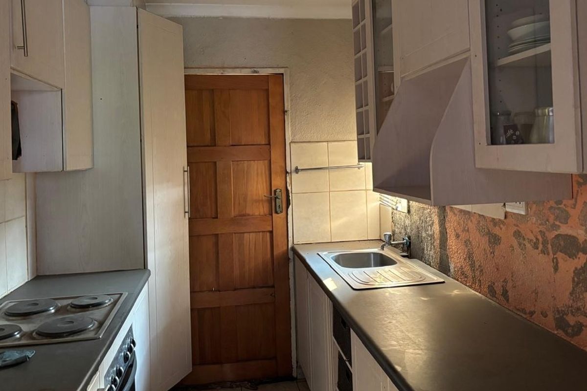 A compact kitchen featuring built-in cabinetry, laminate countertops, a stainless steel sink, and an integrated electric hob with oven.
