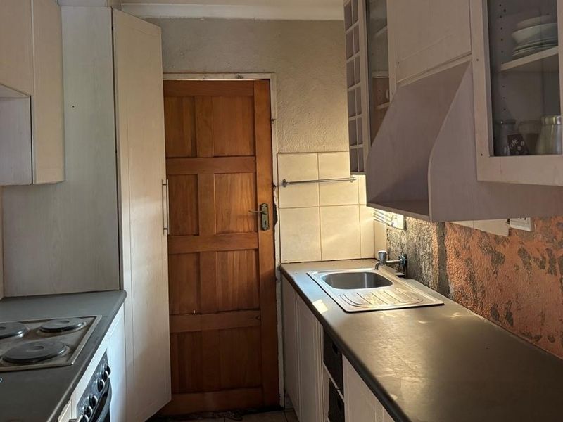 A compact kitchen featuring built-in cabinetry, laminate countertops, a stainless steel sink, and an integrated electric hob with oven.