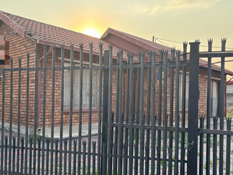 Front view of a face brick house featuring a tiled roof, paved driveway, and secure metal perimeter fencing.
