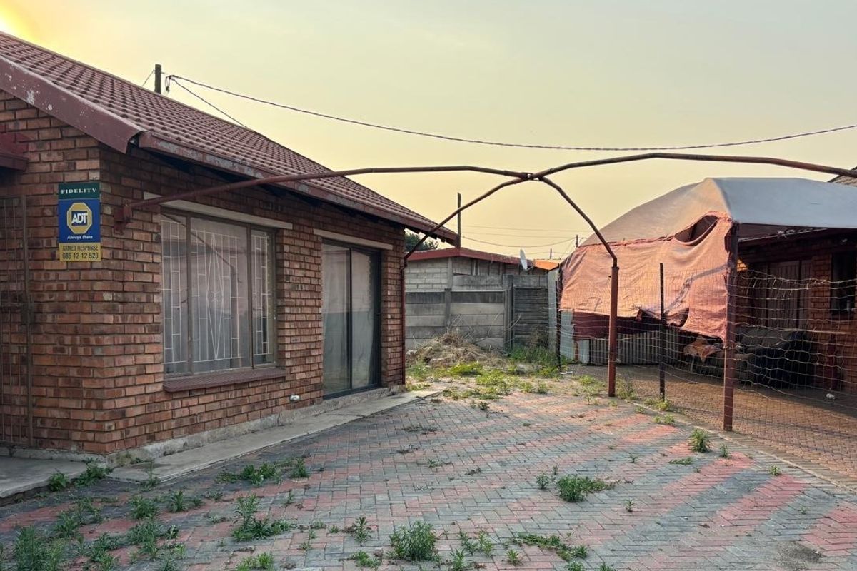 Rear exterior view of a face brick house featuring a paved area and a metal carport structure requiring maintenance.