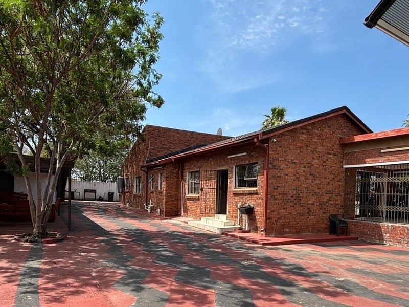 Rear view of a face brick house featuring a large paved driveway area and a covered patio space.