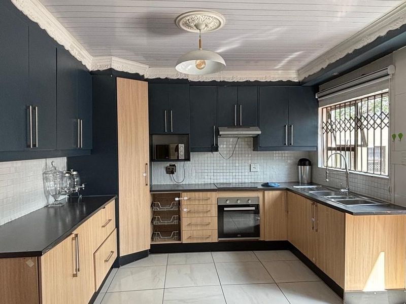Modern kitchen featuring two-tone cabinetry, built-in oven and hob, extractor fan, tiled backsplash, and ample counter space with a double sink.