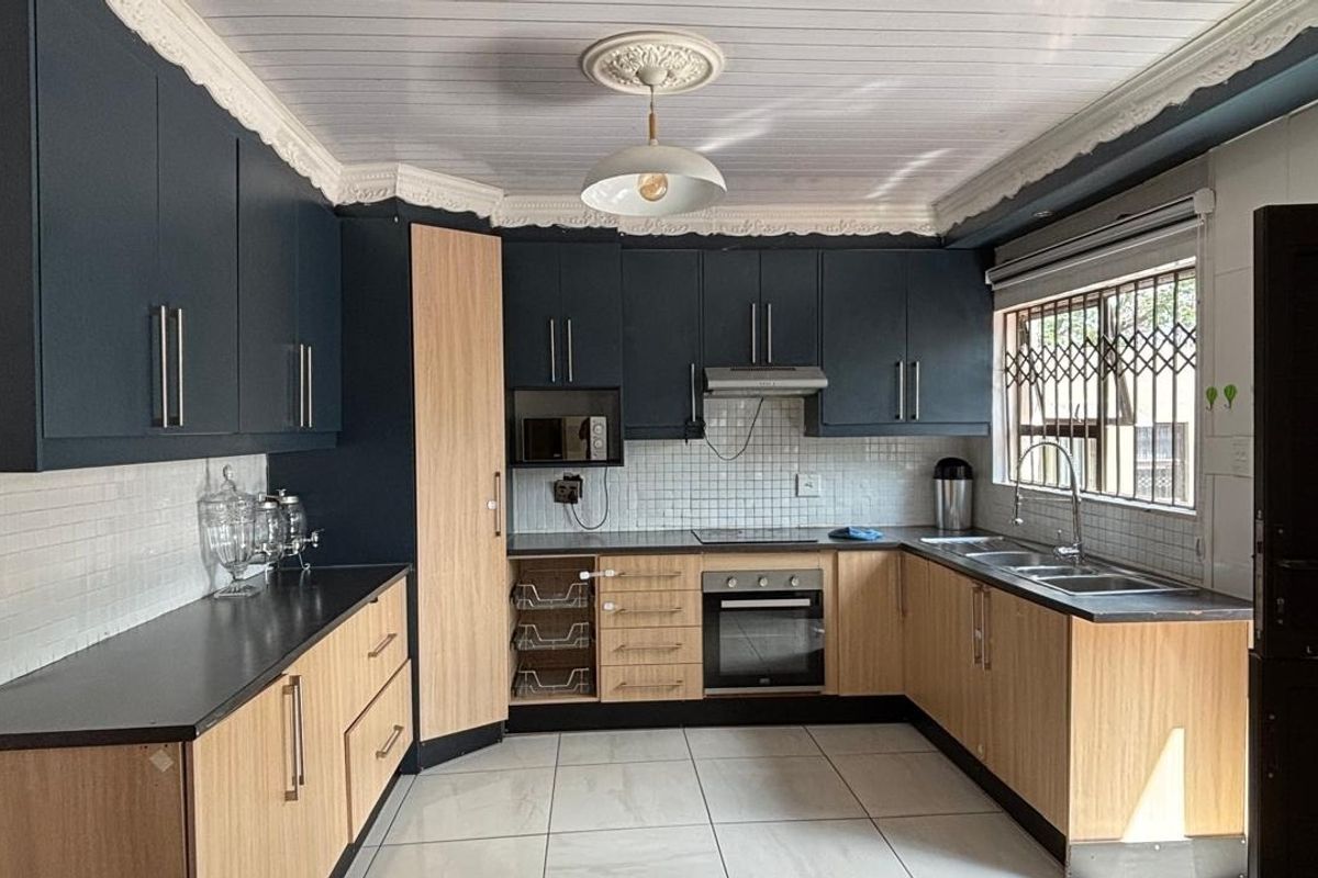 Modern kitchen featuring two-tone cabinetry, built-in oven and hob, extractor fan, tiled backsplash, and ample counter space with a double sink.