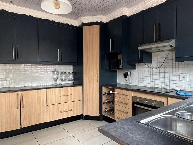 Modern kitchen featuring two-tone cabinetry, tiled backsplash, built-in oven with extractor fan, and a double sink with a gooseneck faucet.