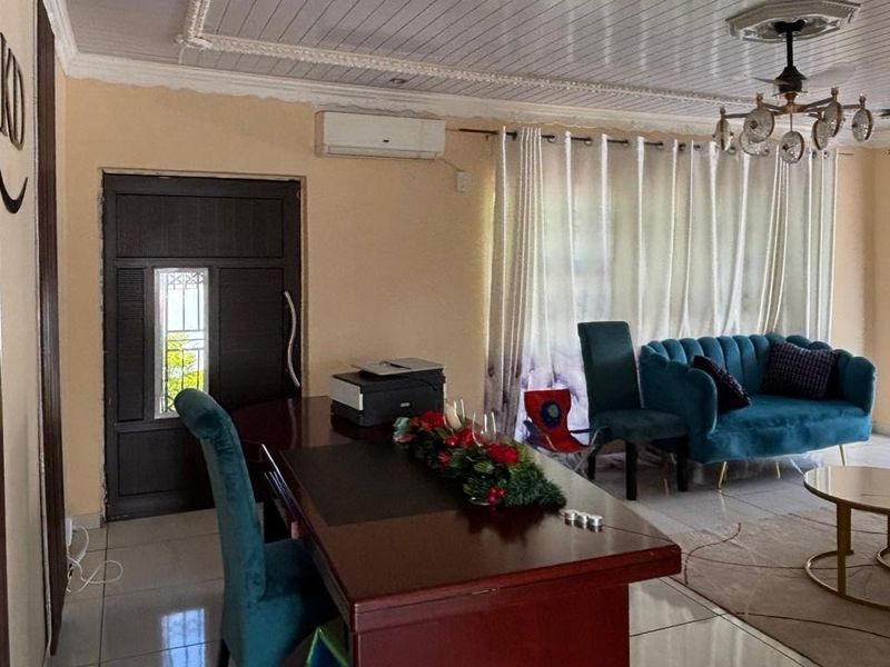 A living room featuring tiled flooring, a ceiling fan, decorative ceiling molding, and a wall-mounted air conditioning unit.