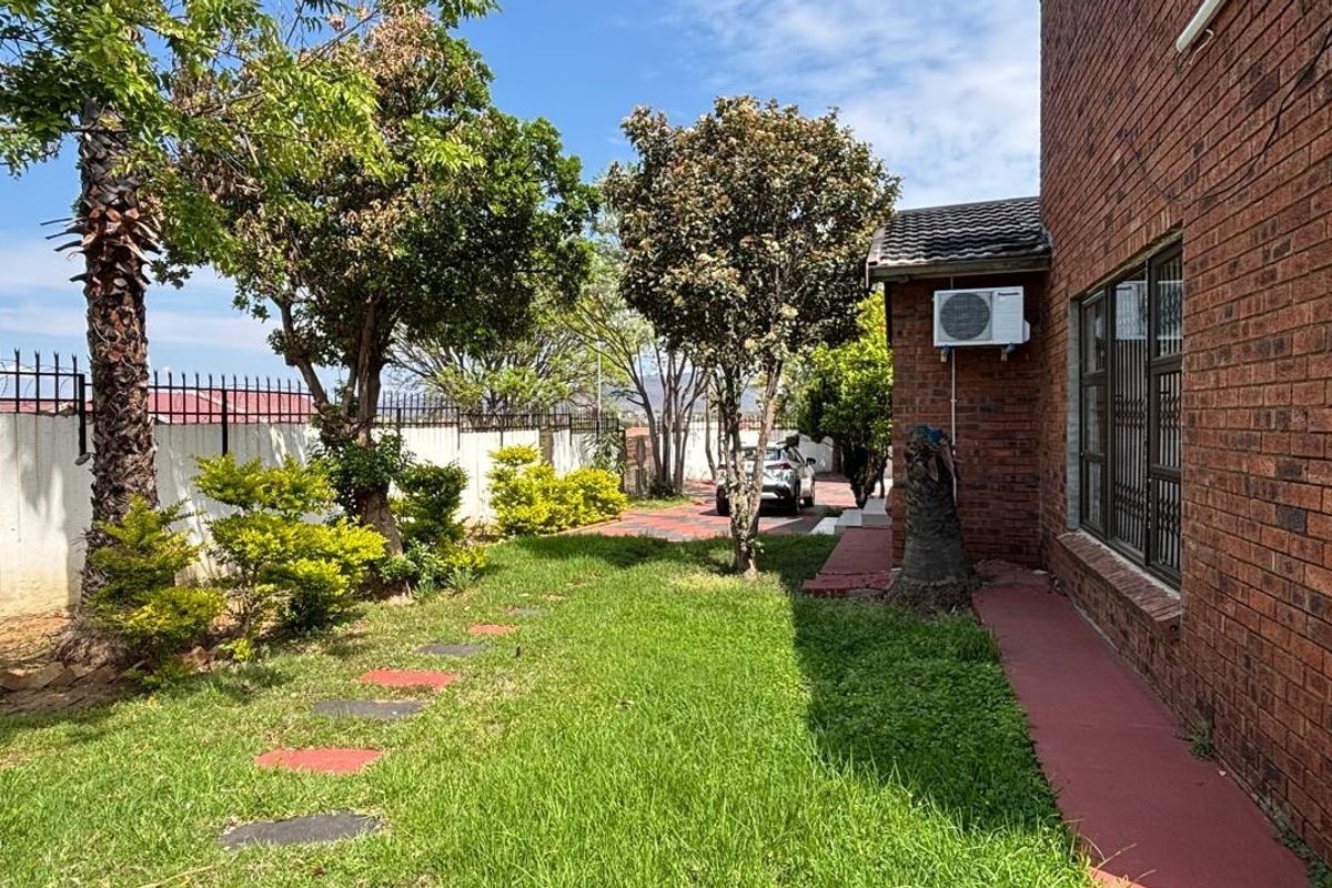 A side view of the property featuring a face brick exterior, a small lawn, paved walkway, and perimeter security fencing.