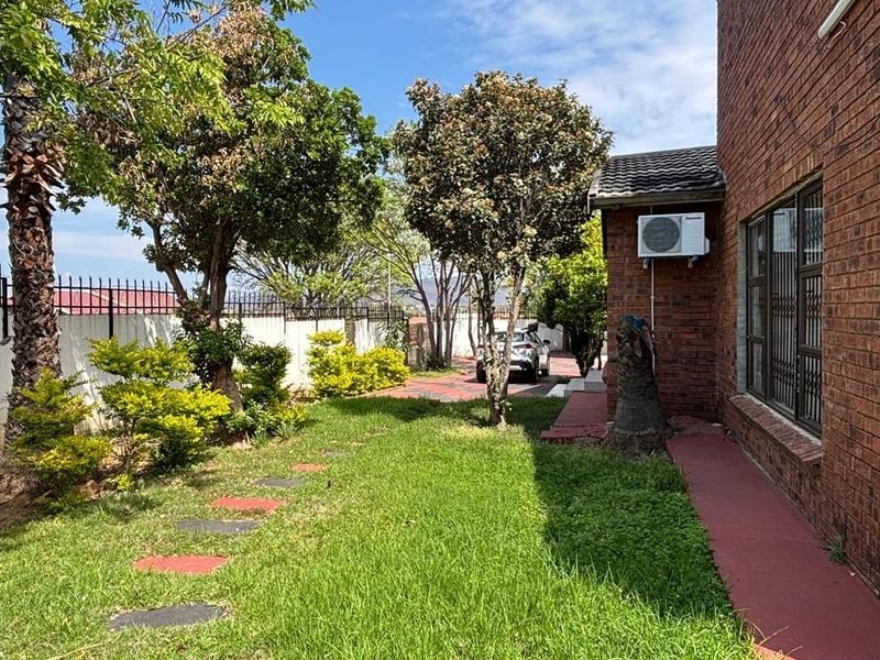 A side view of the property featuring a face brick exterior, a small lawn, paved walkway, and perimeter security fencing.