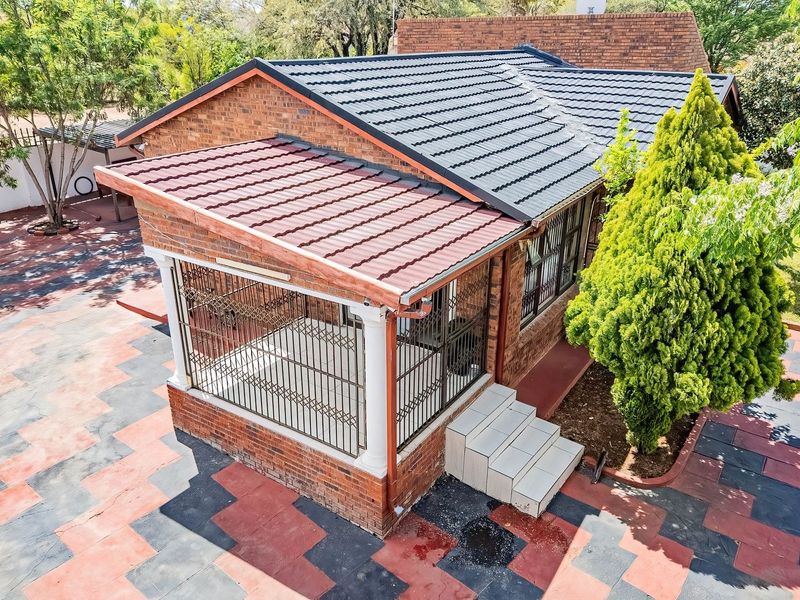 Aerial view of the rear exterior featuring a brick facade, covered patio with security gates, and extensive paved outdoor area.