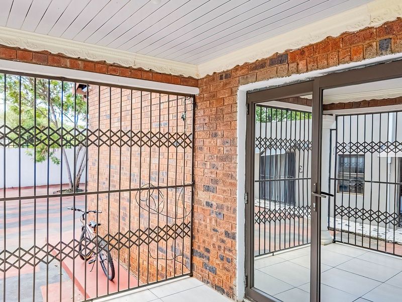 A covered patio area featuring exposed brick walls, tiled flooring, and secure metal gates, providing a functional outdoor transition space.