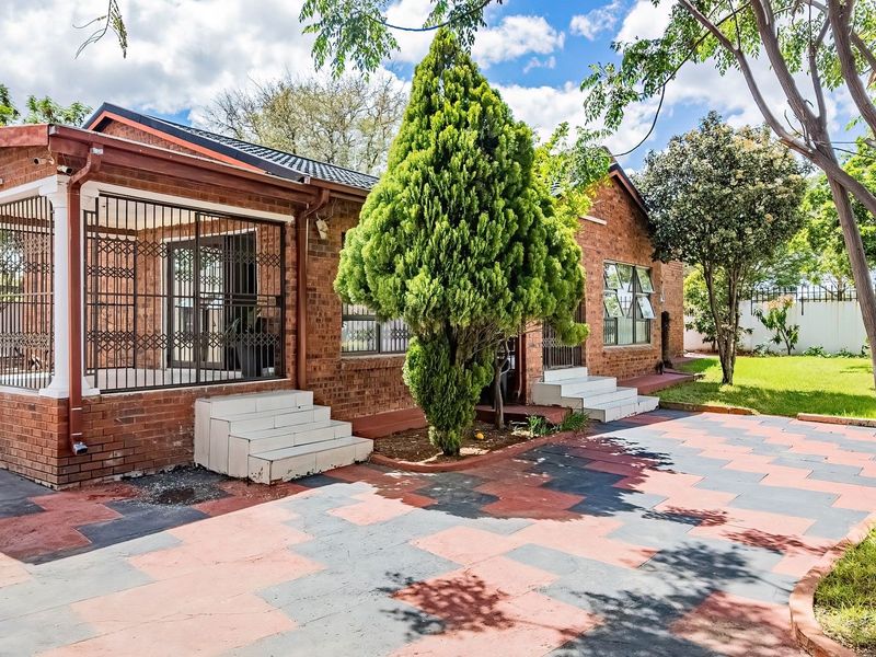 Rear view of a face brick house featuring a paved courtyard, tiled patio area with security gates, and established garden surroundings.