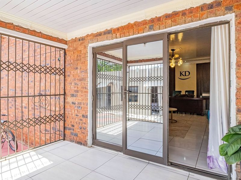 A covered patio area featuring exposed brick walls, tiled flooring, and sliding glass doors providing access to the interior living space.