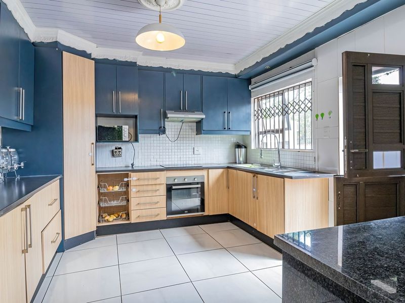 A functional kitchen featuring two-tone cabinetry, built-in oven and hob, tiled backsplash, and a double sink with a security gate on the window.