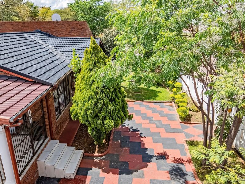 An elevated view of the rear exterior featuring a brick house with a tiled roof, a patterned paved patio, and a landscaped garden area.
