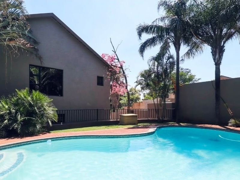 A private outdoor pool area featuring a curved swimming pool, brick paved surround, and established garden landscaping with perimeter walling.