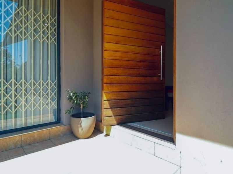 A modern entrance featuring a large timber pivot door and a secure metal gate, leading into the home from a tiled porch area.