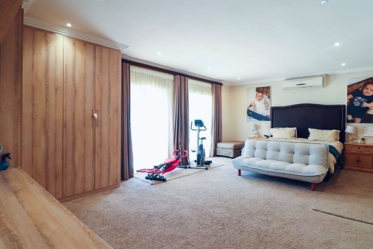 Spacious bedroom featuring extensive built-in cupboards, carpeted flooring, recessed lighting, an air conditioning unit, and sliding glass doors leading to the exterior.