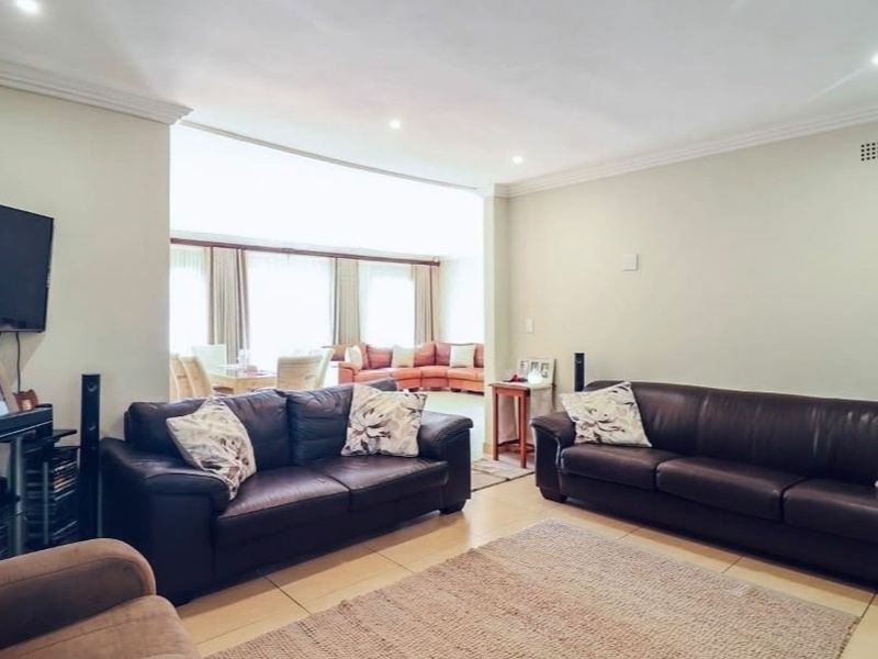 Spacious open-plan living area featuring neutral tiled flooring, recessed downlighting, and decorative cornicing, creating a bright and versatile living space.