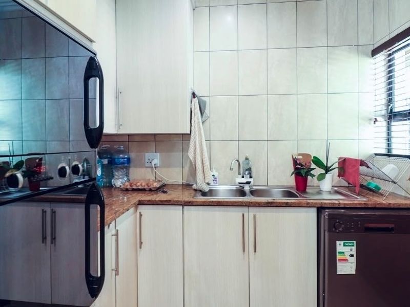 A functional kitchen featuring light-toned cabinetry, granite countertops, a double stainless steel sink, and integrated appliances with tiled wall finishes.