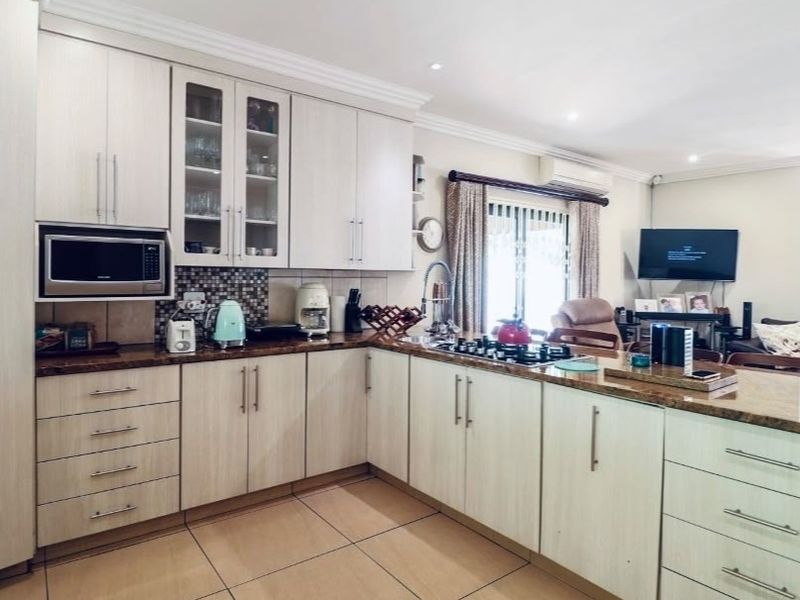 Open-plan kitchen featuring light wood cabinetry, granite countertops, a gas hob, and built-in microwave, seamlessly flowing into the adjacent living area.