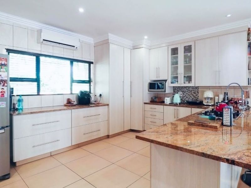 A well-maintained kitchen featuring granite countertops, ample built-in cabinetry, a central island, and tiled flooring, complemented by a split-system air conditioner.