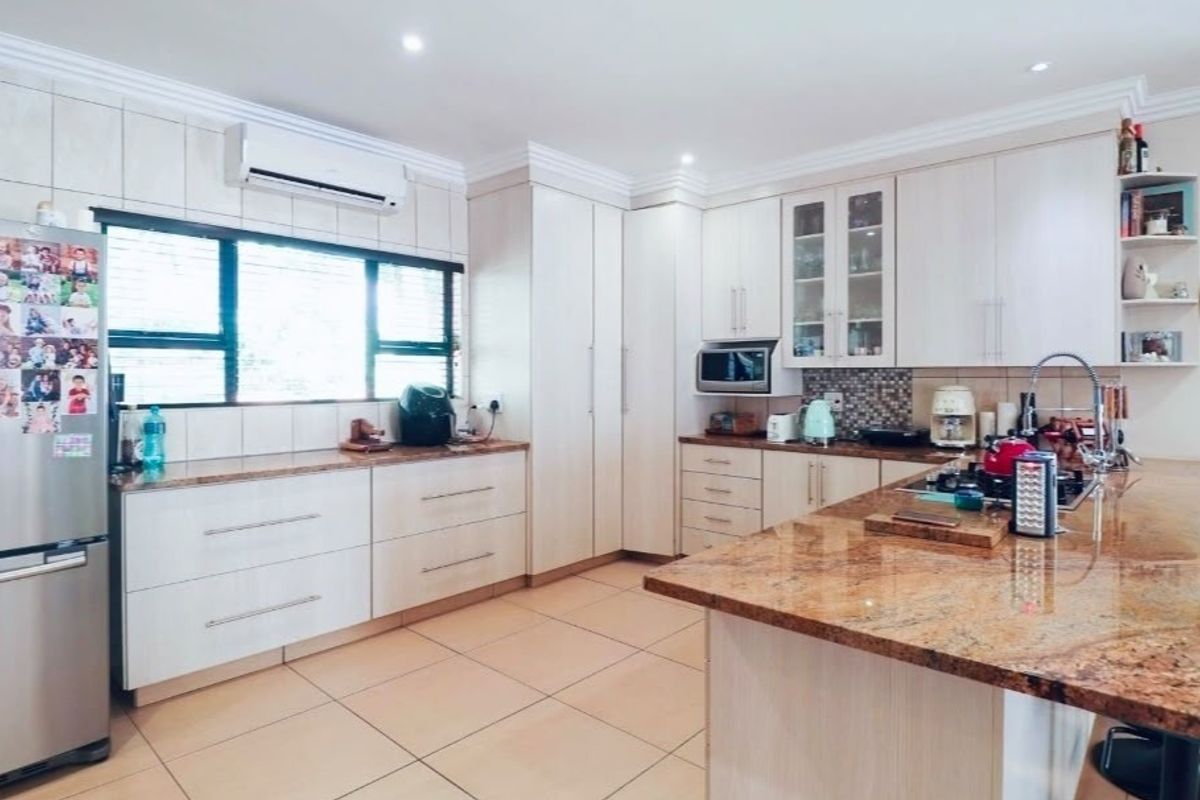 A well-maintained kitchen featuring granite countertops, ample built-in cabinetry, a central island, and tiled flooring, complemented by a split-system air conditioner.