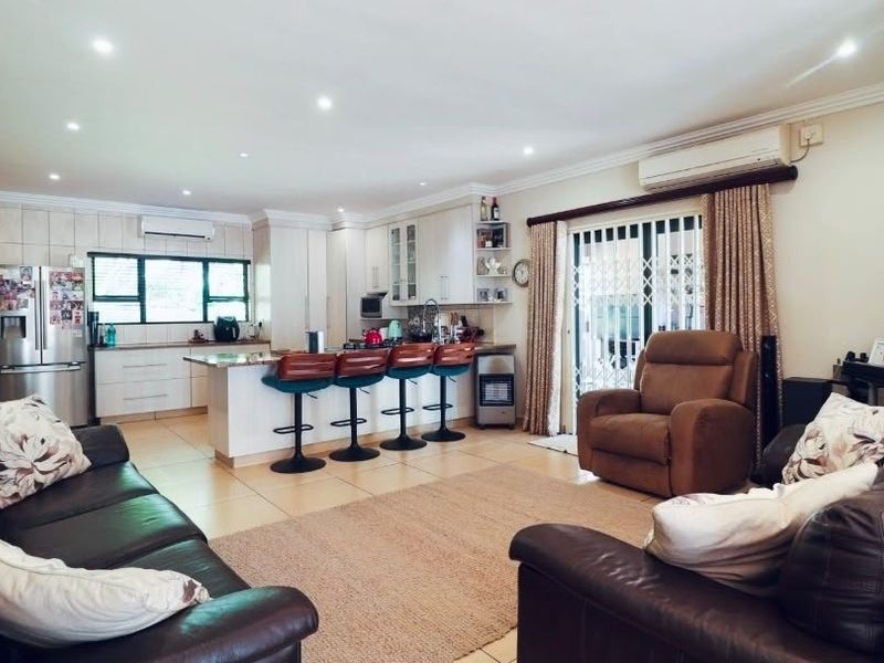 Spacious open-plan living area featuring a modern kitchen with stone countertops, tiled flooring, recessed lighting, and direct access to the outdoor area.