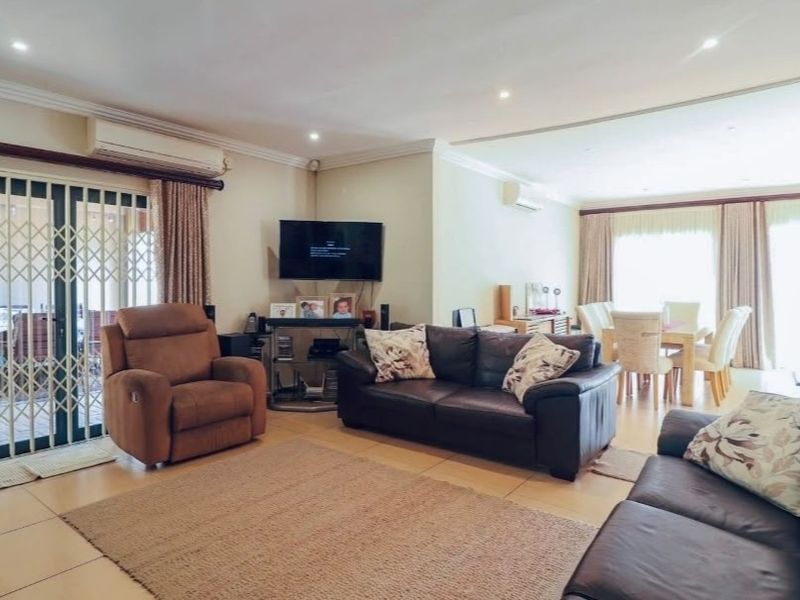 Spacious open-plan living and dining area featuring tiled flooring, recessed lighting, and sliding glass doors leading to an outdoor patio.
