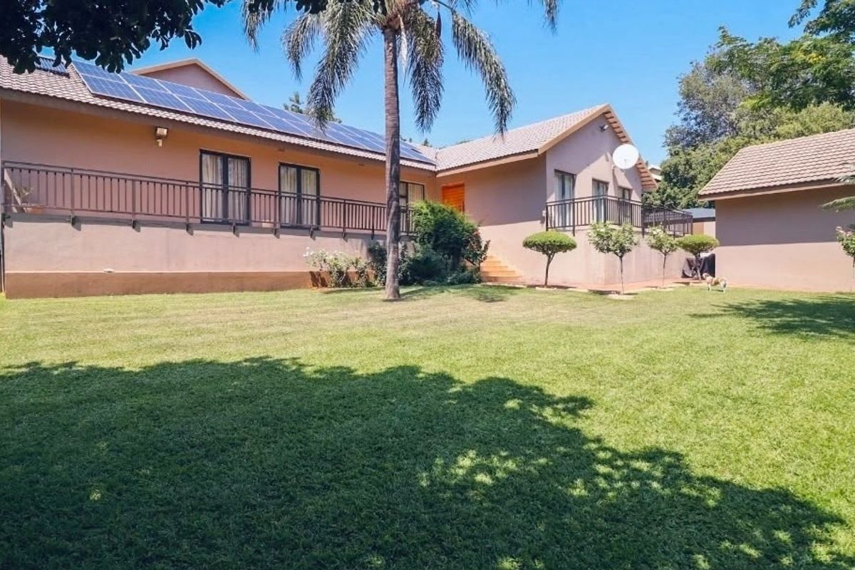 Rear view of the house featuring a spacious lawn, solar panel installation on the roof, and a raised patio area with metal railings.