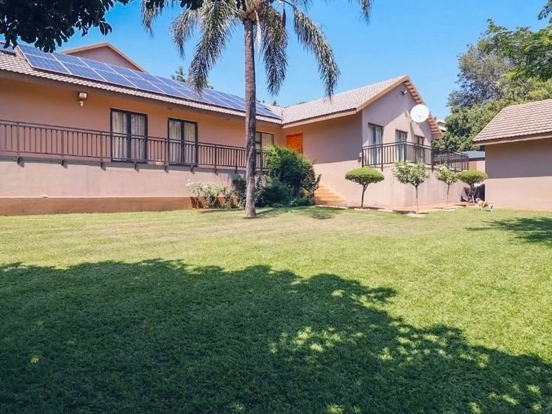 Rear view of the house featuring a spacious lawn, solar panel installation on the roof, and a raised patio area with metal railings.