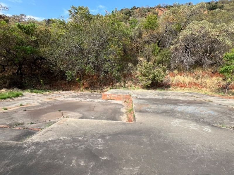 A vacant residential plot featuring an existing concrete slab foundation and brick retaining wall, set against a natural hillside backdrop.