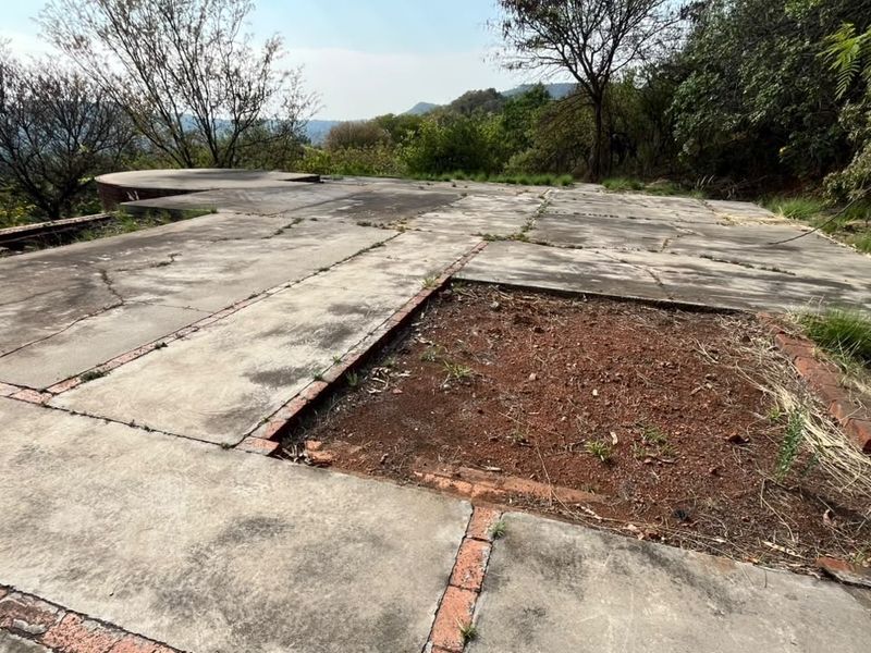 A vacant residential plot featuring an existing concrete slab foundation with brick edging, set against a natural landscape background.