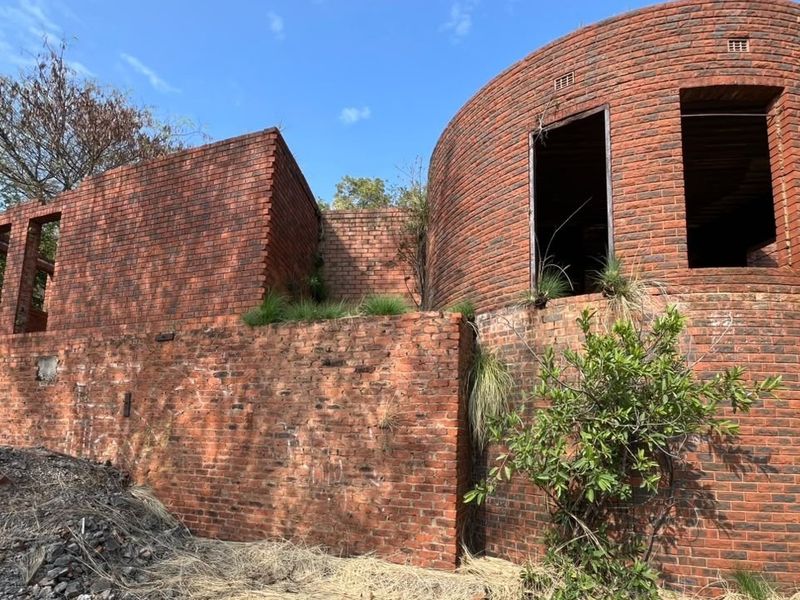 A partially constructed residential structure featuring unique curved brick walls and open window apertures, currently in a shell state requiring completion.