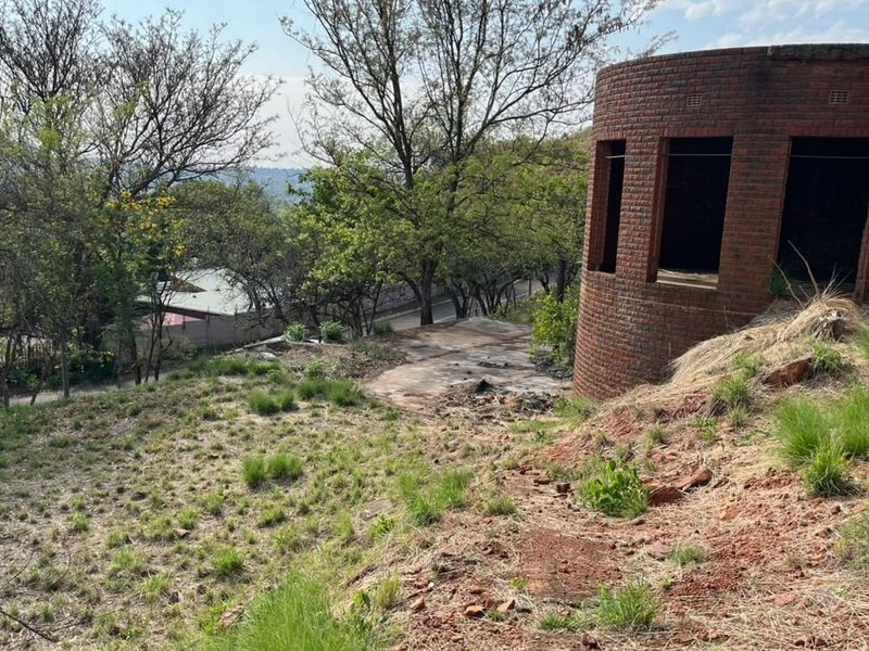 A view of a sloped residential plot featuring an unfinished circular brick structure and natural vegetation.
