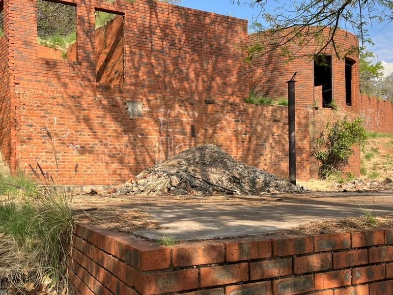 View of an unfinished brick structure on a residential plot, featuring exposed masonry walls and a concrete foundation base.