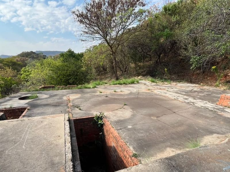 A vacant residential plot featuring a weathered concrete slab foundation and exposed brick retaining walls set against a natural hillside backdrop.
