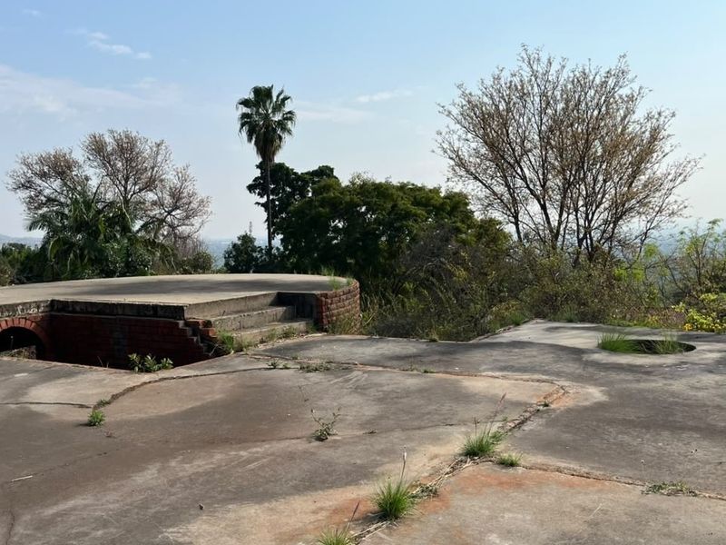An elevated concrete platform with brick retaining walls and stairs, set within a natural landscape, showing signs of weathering and structural wear.