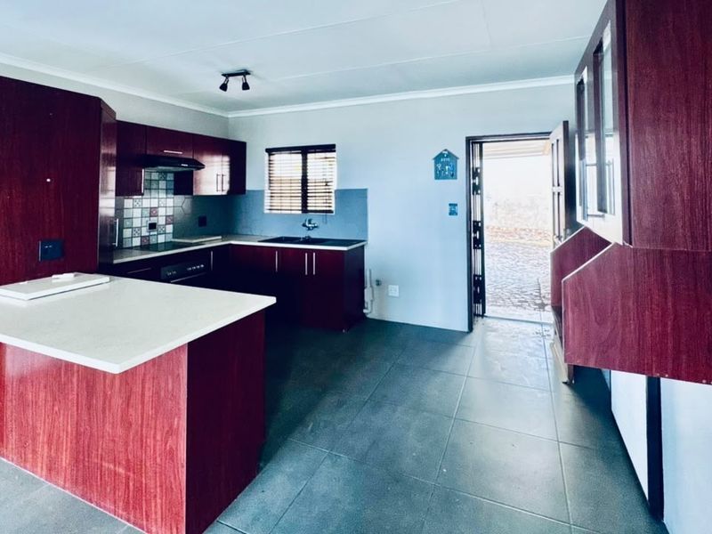 A functional kitchen featuring dark wood-look cabinetry, a central island, tiled flooring, and direct access to an outdoor area through a security gate.