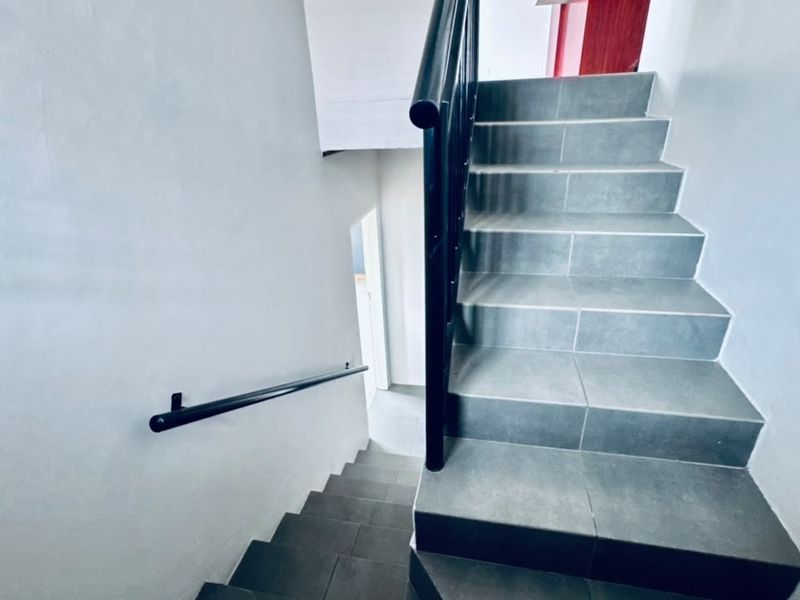 A clean, modern staircase featuring grey tiled steps and a black metal handrail, providing access between levels in the townhouse.