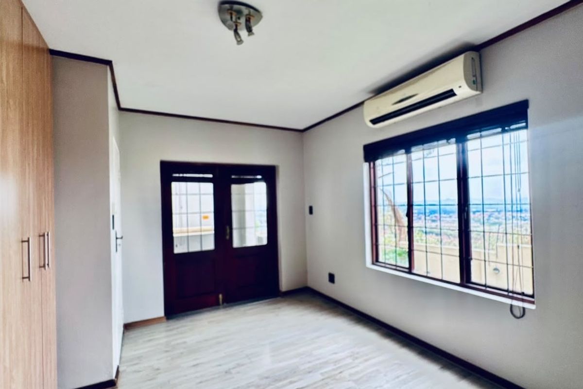 A bright, empty bedroom featuring laminate flooring, built-in cupboards, a wall-mounted air conditioning unit, and security bars on the windows.