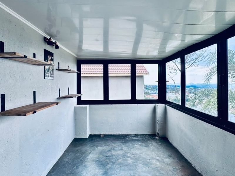 An enclosed balcony or sunroom featuring large windows with views, fixed wall shelving, and a clean, minimalist aesthetic.