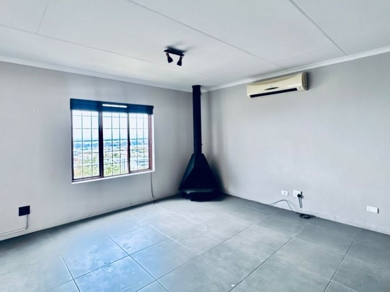 An empty living room featuring tiled flooring, a built-in fireplace, and a wall-mounted air conditioning unit with views through a security-barred window.