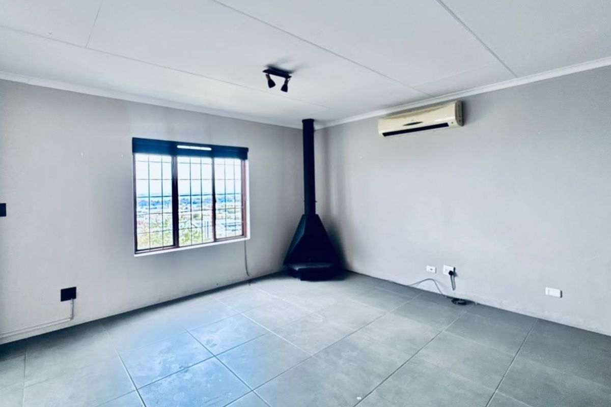 An empty living room featuring tiled flooring, a built-in fireplace, and a wall-mounted air conditioning unit with views through a security-barred window.