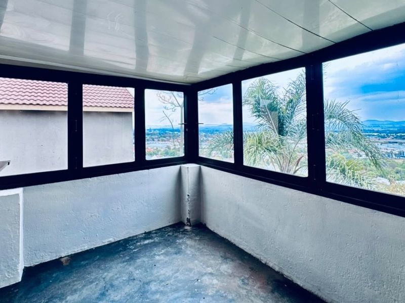 Enclosed balcony or sunroom featuring large windows with panoramic views, black frames, and built-in shelving, offering a versatile space for relaxation.