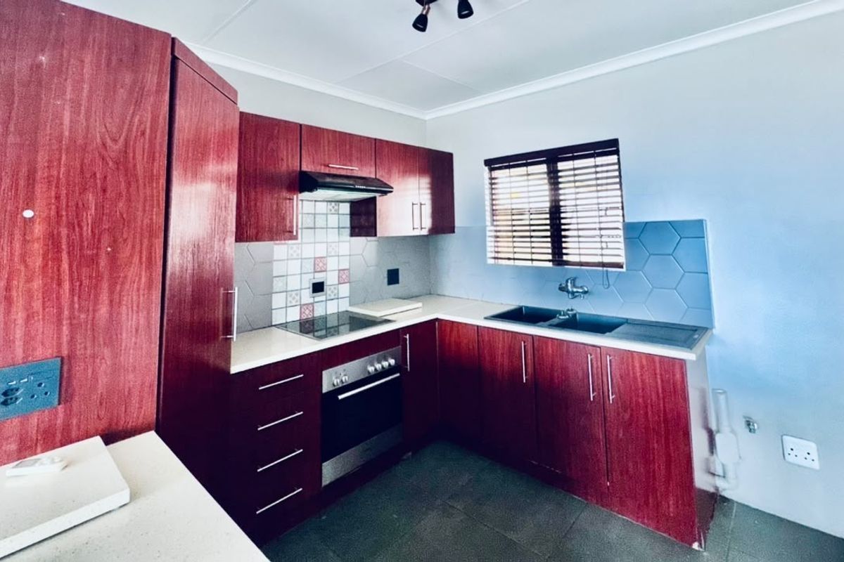 A functional kitchen featuring dark wood-finish cabinetry, integrated oven and hob, tiled splashbacks, and a double sink with a window view.